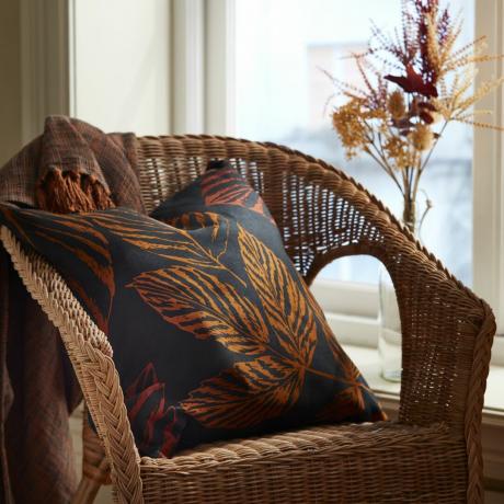 cuscino decorativo autunnale su sedia in rattan con fiori secchi in un vaso in colori autunnali
