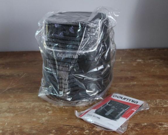 Digitale 4-Liter-Luftfritteuse von Gourmia, verpackt in einer Plastikverpackung, auf einem abgenutzten Holztisch