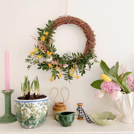 lentekrans die aan de muur hangt met potten met lenteplanten, souvenirs en kaarsen