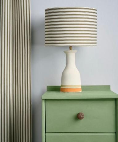 Una lampada bianca con paralume a righe su una cassettiera verde