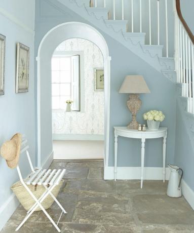 Idées de peinture d'escalier par Little Greene utilisant de la peinture bleu clair, une chaise blanche et une console dans le couloir avec une décoration murale à cadre photo argenté, des fleurs et un décor d'éclairage d'abat-jour beige