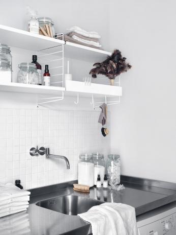 Unidad de estantería de hilo blanco en un lavadero o cocina encima de un fregadero de acero inoxidable