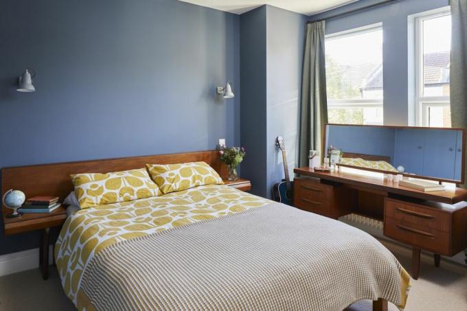 Un dormitorio con muebles de mediados de siglo y paredes de color azul oscuro.