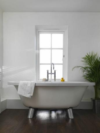 piccola vasca da bagno indipendente in un bagno piccolo con ampia finestra e combinazione di colori bianca