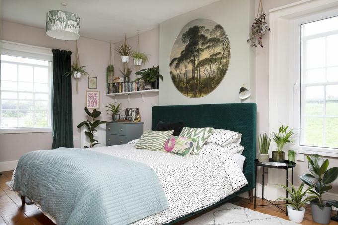 Schlafzimmer mit blassrosa und grünen Wänden, grünem Samtkopfteil, fleckiger weißer und schwarzer Bettwäsche und botanischen Kunstwerken