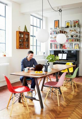 रंगीन रंगों में ईम्स कुर्सियों के साथ एक मेज पर बैठे कार्लो विसिओन