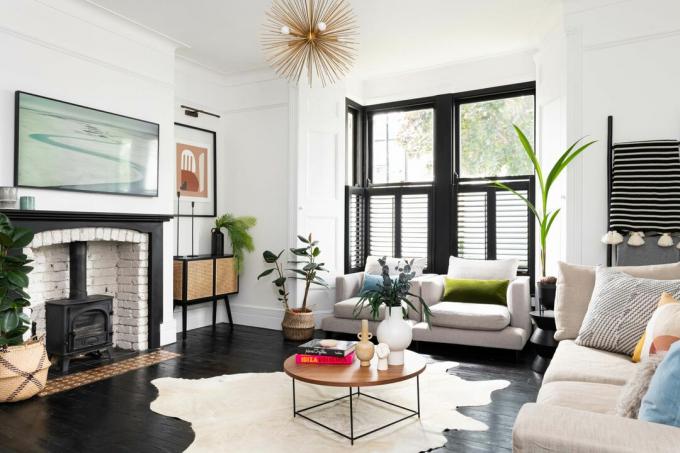 Schwarz-weißes Wohnzimmer mit schwarzem Bodenbelag, schwarz gestrichenem Fenster, beigen Sofas, Teppich, Couchtisch, Pflanzen, Kunstwerken, Holzofen