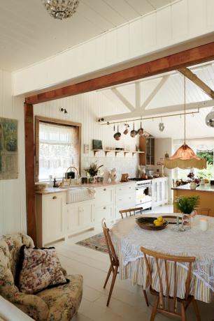 bucătărie/sufragerie rustică cu parchet vopsit în alb, unități de bucătărie albe, grinzi, shiplap, imprimeuri florale