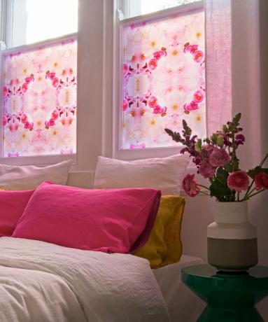 ピンクのデカールが貼られた窓の下にピンクのクッションが置かれたベッド