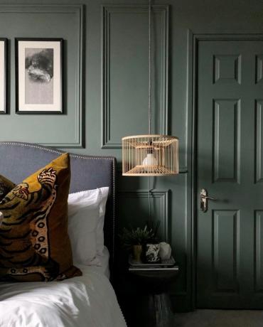 Ein grün getäfeltes Schlafzimmer mit hängender Seitenlampe und gerahmter monochromer Wandkunst