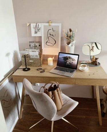 Puinen kirjoituspöytä vaaleanpunaisella tuolilla ja seinätaidetta