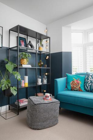 Ruang tamu dengan setengah biru, sofa beludru biru cerah, dan unit rak hitam dengan tanaman, vas, dan ornamen lainnya