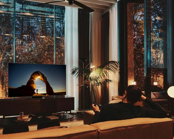 Moški gleda Samsungov televizor The Frame ponoči z odprtimi žaluzijami