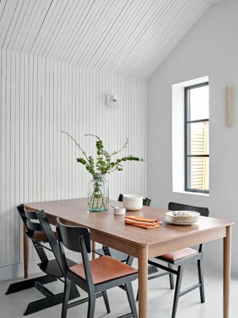 Drevený jedálenský stôl a čierne stoličky na stene z bieleho lamelového panelu