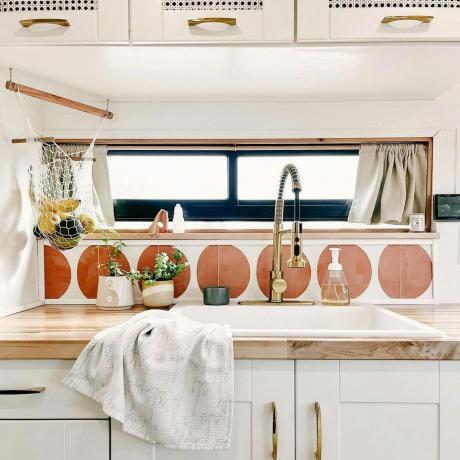 Kjøkkenvask med bakplate av fliser, bronzegold armaturer og krem ​​skap