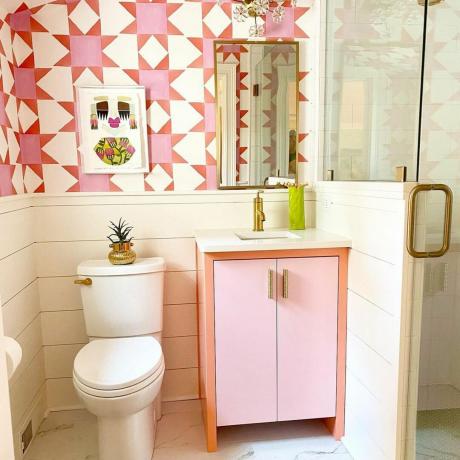 Baño pequeño e impactante con lindo tocador de dos tonos y gráfico coordinado, papel tapiz estampado rosa