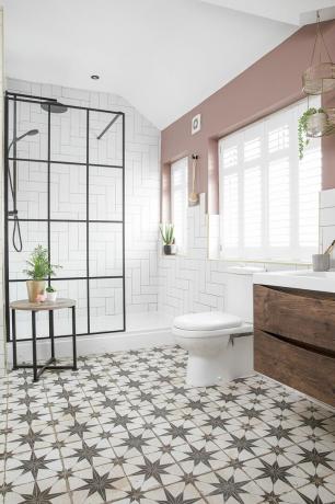 Kylpyhuoneessa kuviollinen laattalattia, Crittal-tyylinen suihkuseinä, valkoinen wc ja puinen alaosa ja vaaleanpunaiset seinät