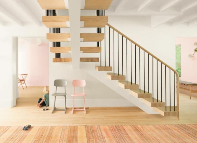 Holztreppe mit Metallspindeln, offenes Wohnzimmer, Holzboden, weiße Wände, gestreifter Teppich