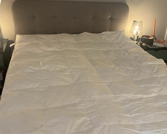 DUSK Supreme-Gänsedaunen-Matratzenauflage auf dem Bett mit hellgrauem Kopfteil und Lampen daneben