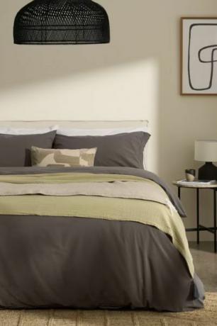 made.com ベッドの上のグレーの寝具、緑のスローと黒のベッドサイド テーブル 