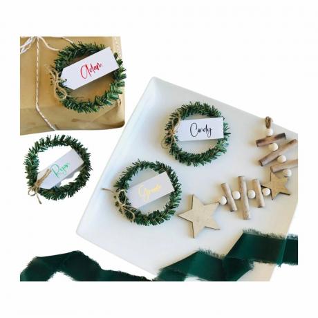 Kalėdų eglutės vietos atvirukai ant baltų lėkščių ir ruda dovana