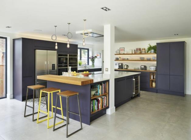 fialová kuchyně s kuchyňským ostrůvkem, otevřenými dřevěnými policemi a dřevěným snídaňovým barem, barové židle, kamenná podlaha