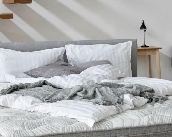 ένα άστρωτο κρεβάτι με γκρι ριχτάρι σε ένα υπνοδωμάτιο σε στυλ Scandi
