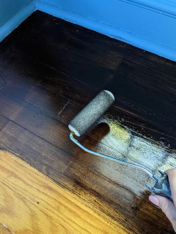 mancha de gel sendo aplicada em um piso de madeira com um rolo de pintura