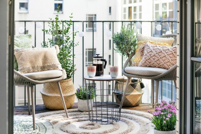 boho stiliaus balkonas su kėdėmis, kilimėliu, pagalvėlėmis, šoniniu stalu, krepšeliais su augalais