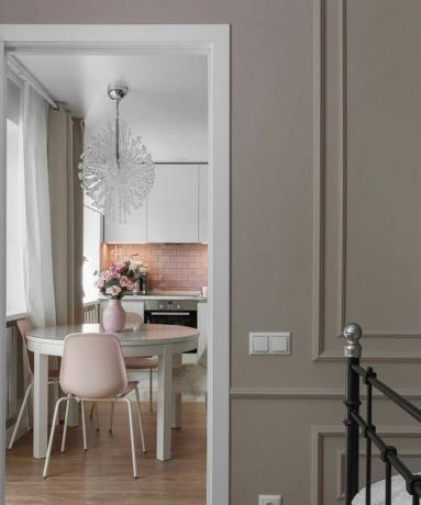 Nápad na stolovanie pre malú kuchyňu so skleneným lustrom, ružovým metrom, bielym okrúhlym stolom, ružovou vázou s kvetmi, ružovými stoličkami a tmavomodrým závesom na okne