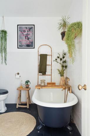 Kamar mandi dengan dinding berubin putih, lantai kayu bercat hitam, bak mandi gulung biru tua, permadani goni, dan aksesoris kayu