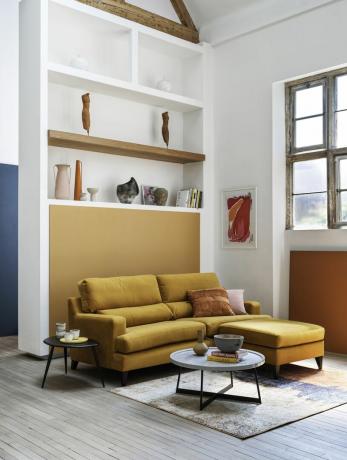 sala de estar com sofá amarelo, mesas laterais redondas, tapete texturizado, estantes, ambiente aberto