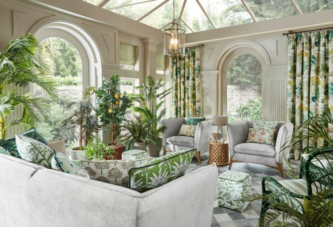 sauļošanās istaba ar čekas grīdu, pelēki dīvāni un atzveltnes krēsli un zaļi botāniskie spilveni un aizkari