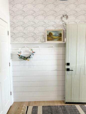 白いシップラップパターンの壁紙と花輪がペグに保持されているアクセントの壁
