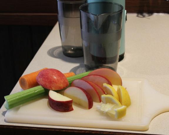 Manzanas, limones, apio y zanahorias en rodajas sobre una tabla de cortar de plástico blanco