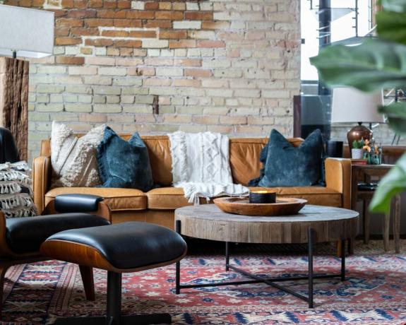 Industriāli lauku stila viesistaba ar apaļkoka un metāla kafijas galdiņu, sinepju dīvānu un atklātu ķieģeļu sienu