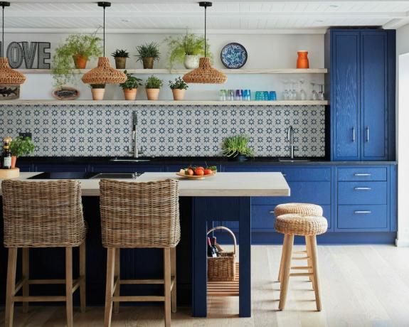 Modré schéma kuchyně s modrým ostrůvkem a skříňkami a vzorovaným modrým obkladem a barovými stoličkami z tkaných materiálů
