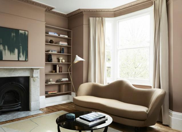 nøytral stue med beige gardiner og teppe, brunfargede vegger og sofa, peis, gulvlampe, kunstverk, svart salongbord