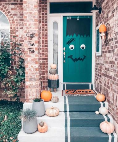 Терасиран дом със зелена врата, украсена на Хелоуин, за да изобрази герой като Франкенщайн с розови тикви