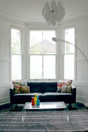 Weißes Erkerfenster mit Milchfolie im Wohnzimmer mit grauem Teppich und blauer Couch