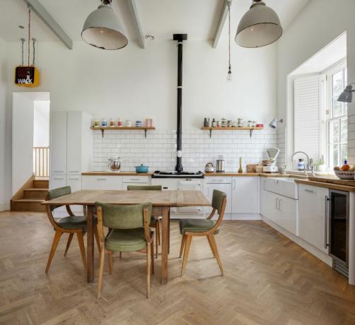 Дрвени кухињски под са кухињским столом и зеленим столицама. Беле јединице са шпоретом