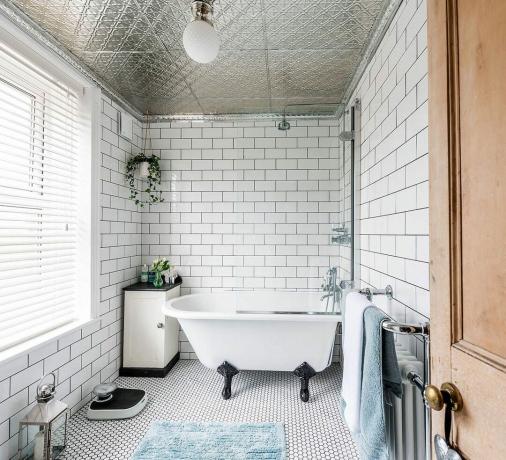 vonios kambarys su baltomis metro plytelėmis, raštuotos grindys, sidabrinės lubos ir mini balta ritininė vonia su juodomis letenėlėmis