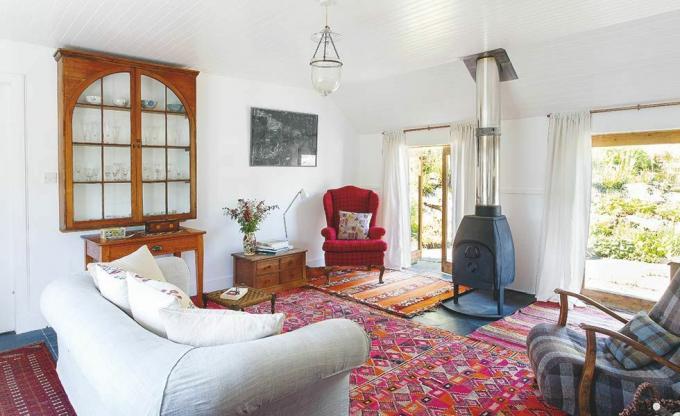 Sala de estar con alfombra roja y silla y estufa de leña en una casa costera