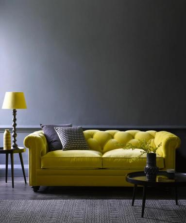 Dramatische moderne woonkamer met donkere houtskoolmuren en vloeren, en pittige citron-fluwelen bank met knopen aan de achterkant.
