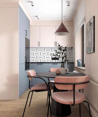 Una zona pranzo in una piccola cucina con tavolo nero arrotondato, sedie rosa e nere, lampada a sospensione a forma di cono rosa, arte murale monocromatica e piastrelle grafiche in bianco e nero