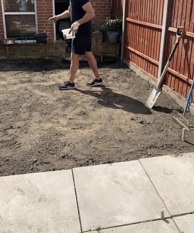 Изображение на мъж, използващ градински валяк, за да опакова почвата и да се отърве от всякакви въздушни джобове в задния двор