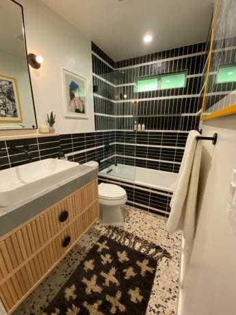 Chuveiro de azulejos pretos com banheira branca. pia e piso de mosaico