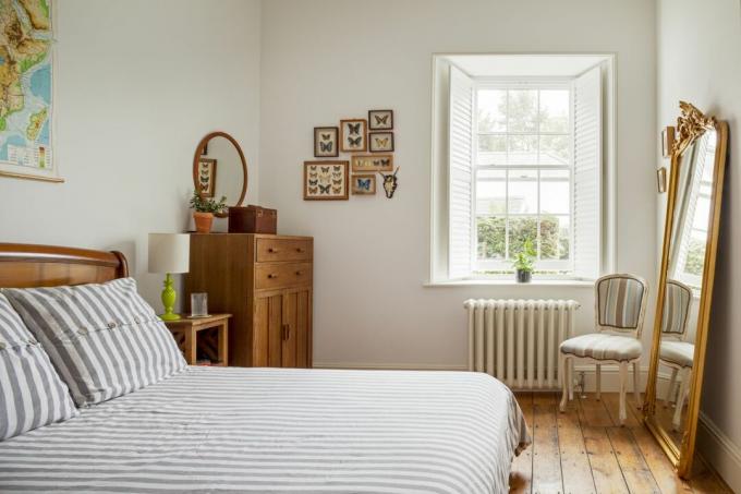 renoviertes Schlafzimmer mit grau-weiß gestreifter Bettwäsche, braunen Holzmöbeln und Fenster