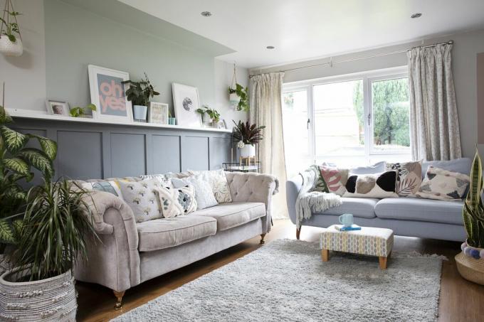 Obývacia izba so sivým obložením až do výšky, pastelovo zelená farba siahajúca nad a na strop cez police, ružová pohovka a sivá pohovka, drevené podlahy a sivý koberec