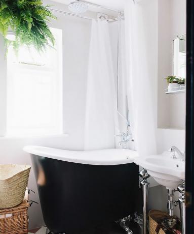 검은색으로 칠해진 욕조, 무늬가 있는 바닥 타일, 샤워 릴에 매달린 고사리가 있는 흰색 욕실